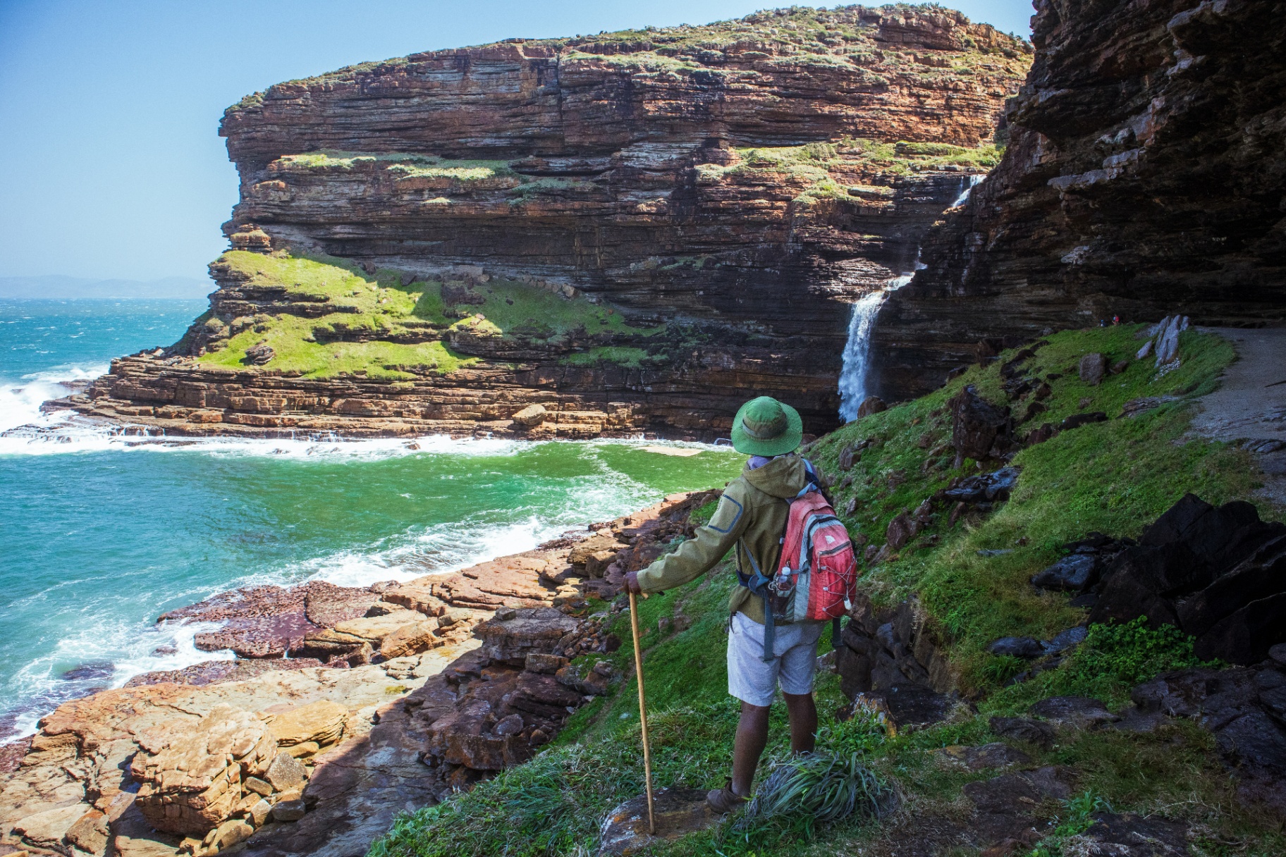 Hiker overlooking a waterfall cascading into a turquoise cove along South Africa's Wild Coast
